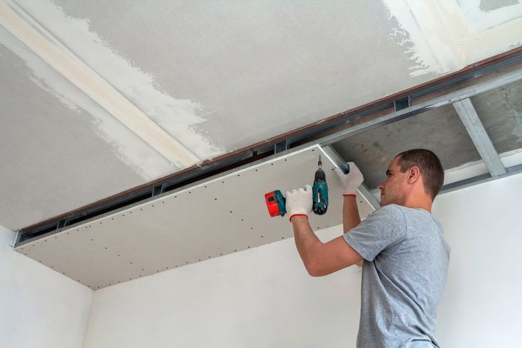 Entreprise de rénovation et d'énergies Calvados - Plaquiste installant des plaques de plâtre sur un chantier.
