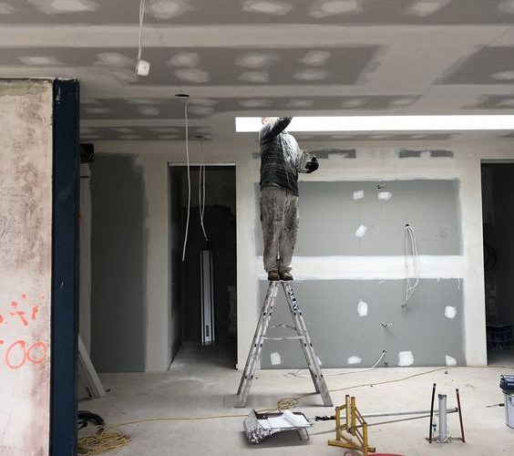 Plaquiste installant des plaques de plâtre sur un chantier. Ce plaquiste est en train de rénover son bien immobilier.