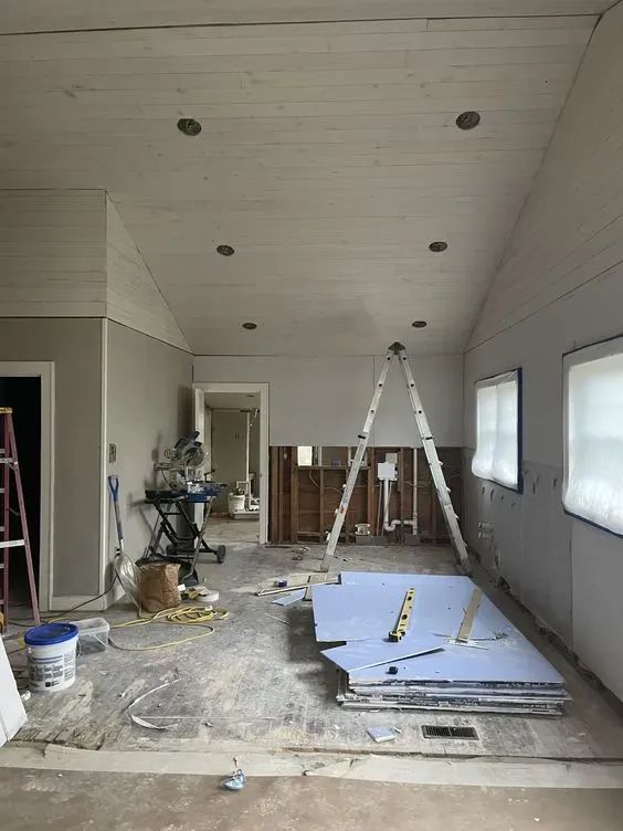 Une pièce en cours de rénovation avec un plafond en bois incliné, des matériaux de construction et des outils éparpillés.